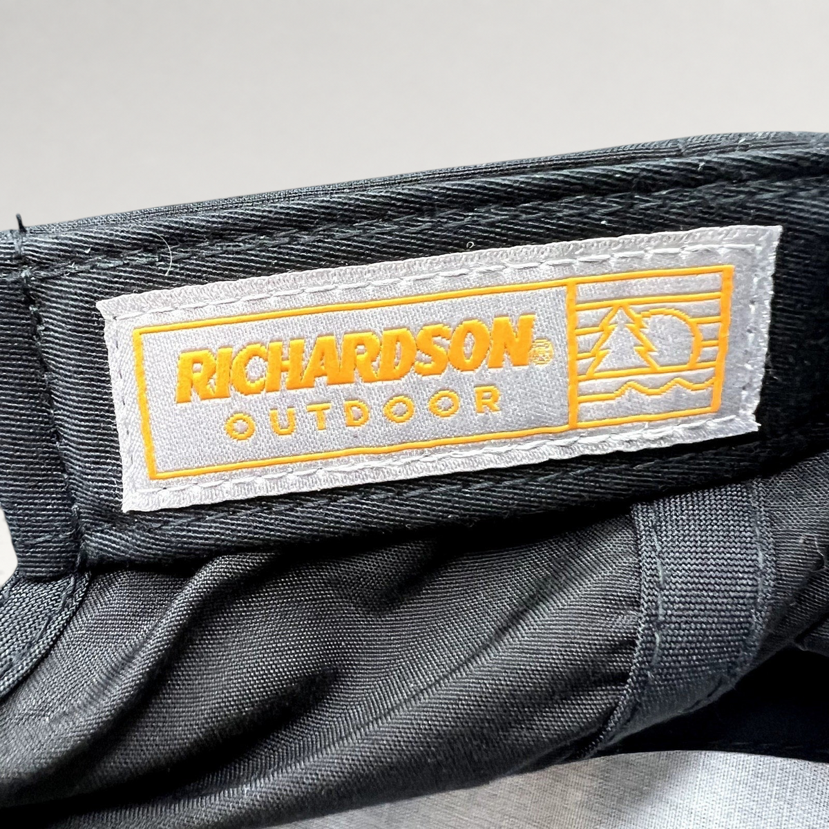Raree Finds Richardson Outdoor label inside a black performance snapback hat with orange and grey branding