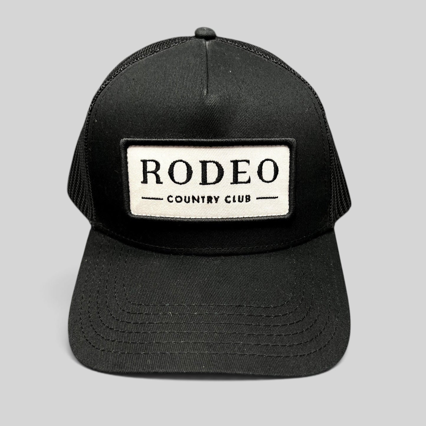 Raree Finds black Rodeo Country Club trucker hat with a white embroidered patch and breathable mesh back panels.
