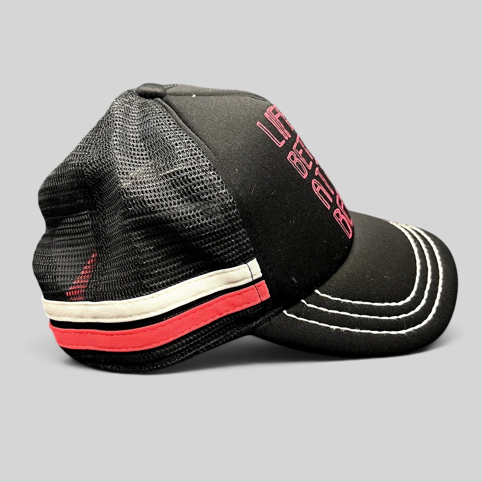 Raree Finds Roxy black trucker hat with pink embroidered text and mesh back, featuring white contrast brim stitching.