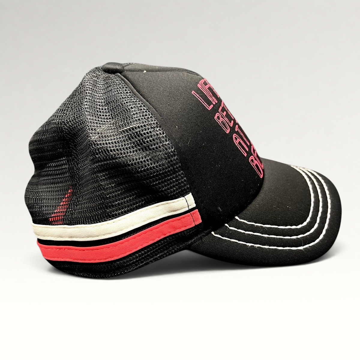 Raree Finds Roxy black trucker hat with pink embroidered text and mesh back, featuring white contrast brim stitching.