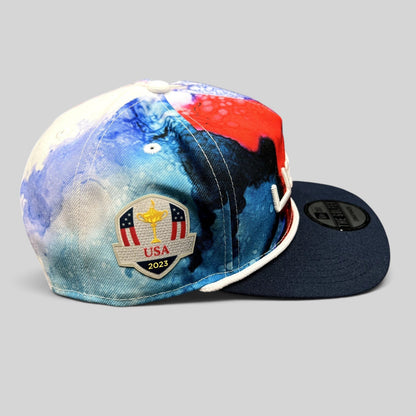 Raree Finds 2023 Ryder Cup Team USA snapback hat with red, white, and blue watercolor print and side tournament patch.