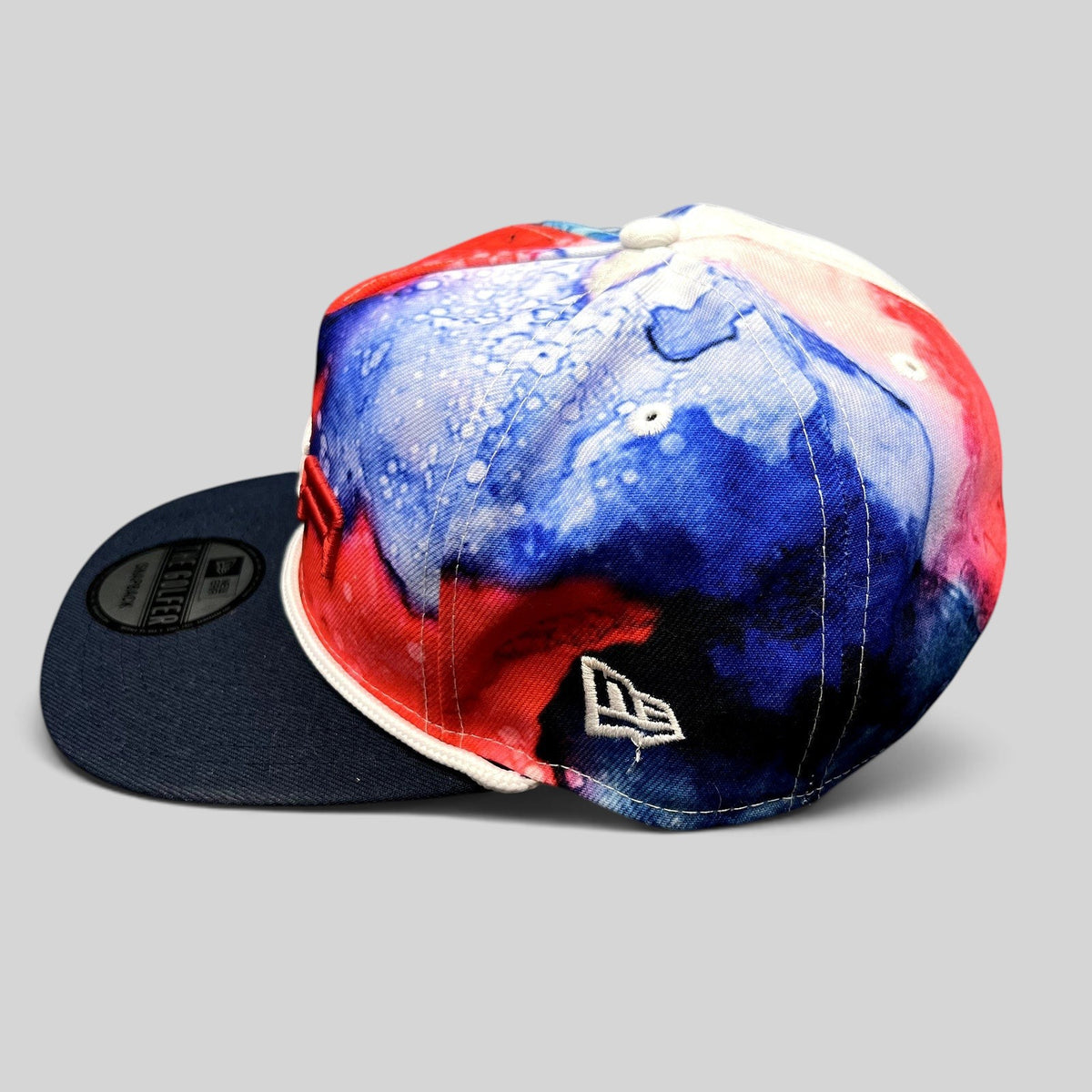Raree Finds 2023 Ryder Cup Team USA snapback hat with red, white, and blue watercolor print and navy brim.