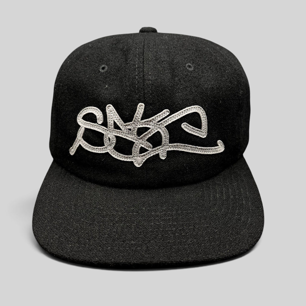 Raree Finds Sake Brand black strapback cap with oversized gray embroidered script logo on a structured wool-blend hat.
