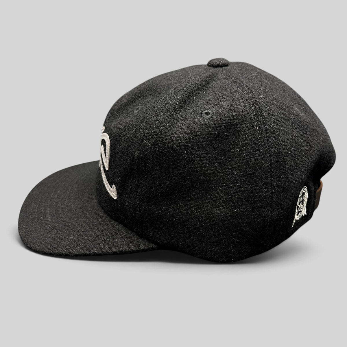 Raree Finds black Sake Brand strapback hat with gray embroidered script logo and flat brim in a side profile view.