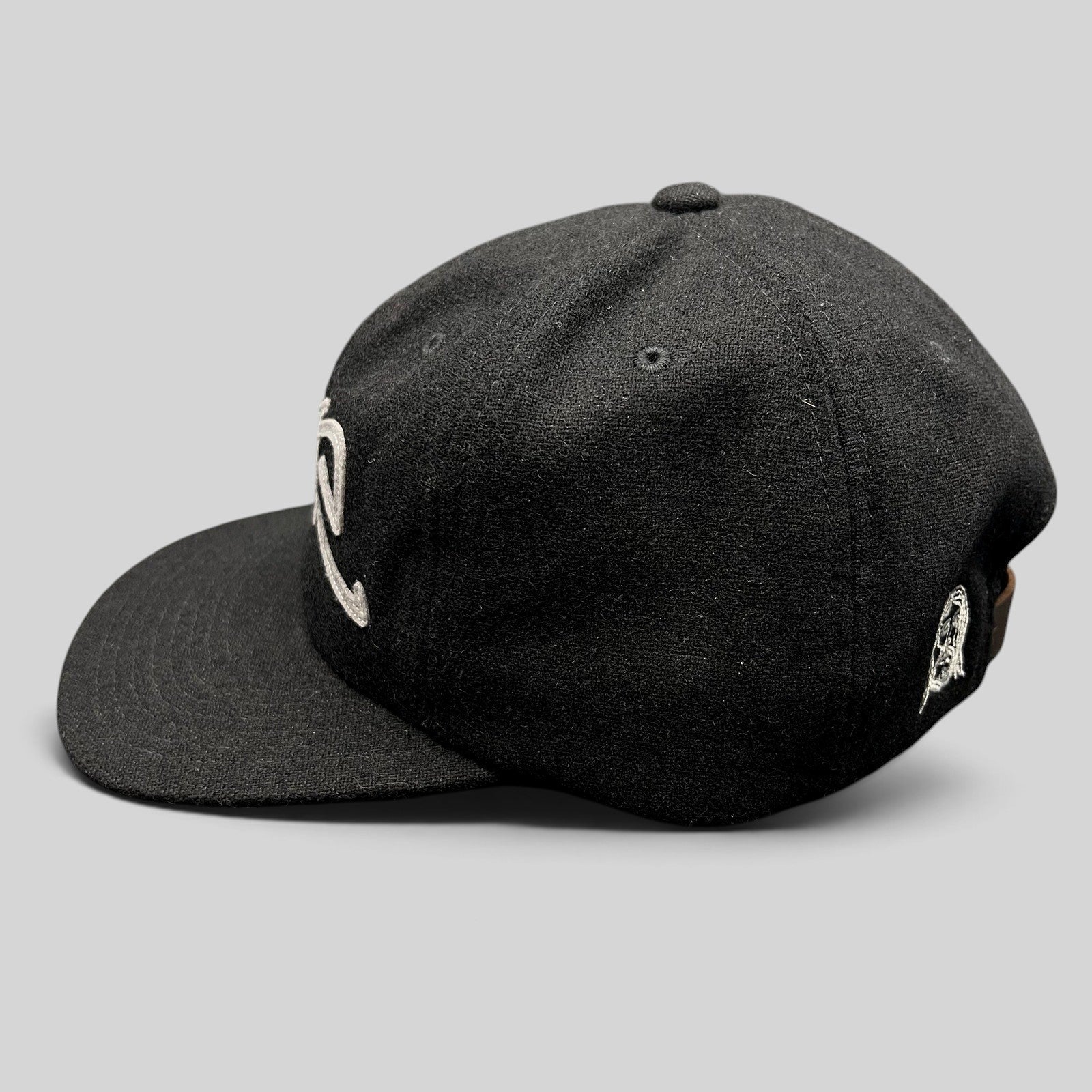Raree Finds black Sake Brand strapback hat with gray embroidered script logo and flat brim in a side profile view.