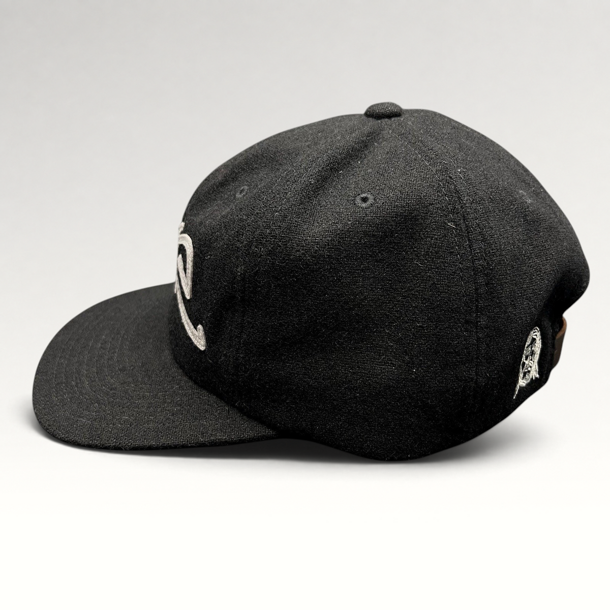 Raree Finds black Sake Brand strapback hat with gray embroidered script logo and flat brim in a side profile view.