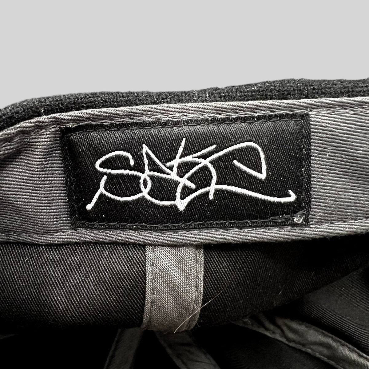 Raree Finds Sake Brand black strapback hat interior featuring a white embroidered script logo label on the crown
