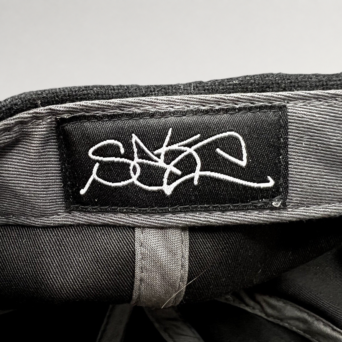 Raree Finds Sake Brand black strapback hat interior featuring a white embroidered script logo label on the crown