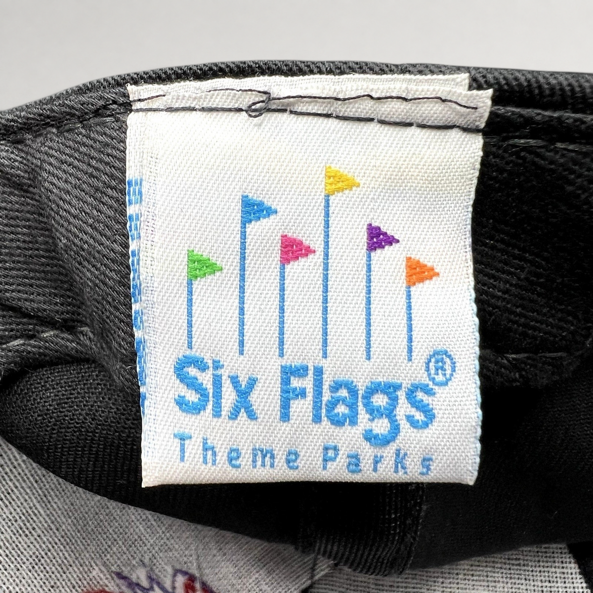 Raree Finds vintage Six Flags Theme Parks woven clothing label with colorful flag icon on black fabric