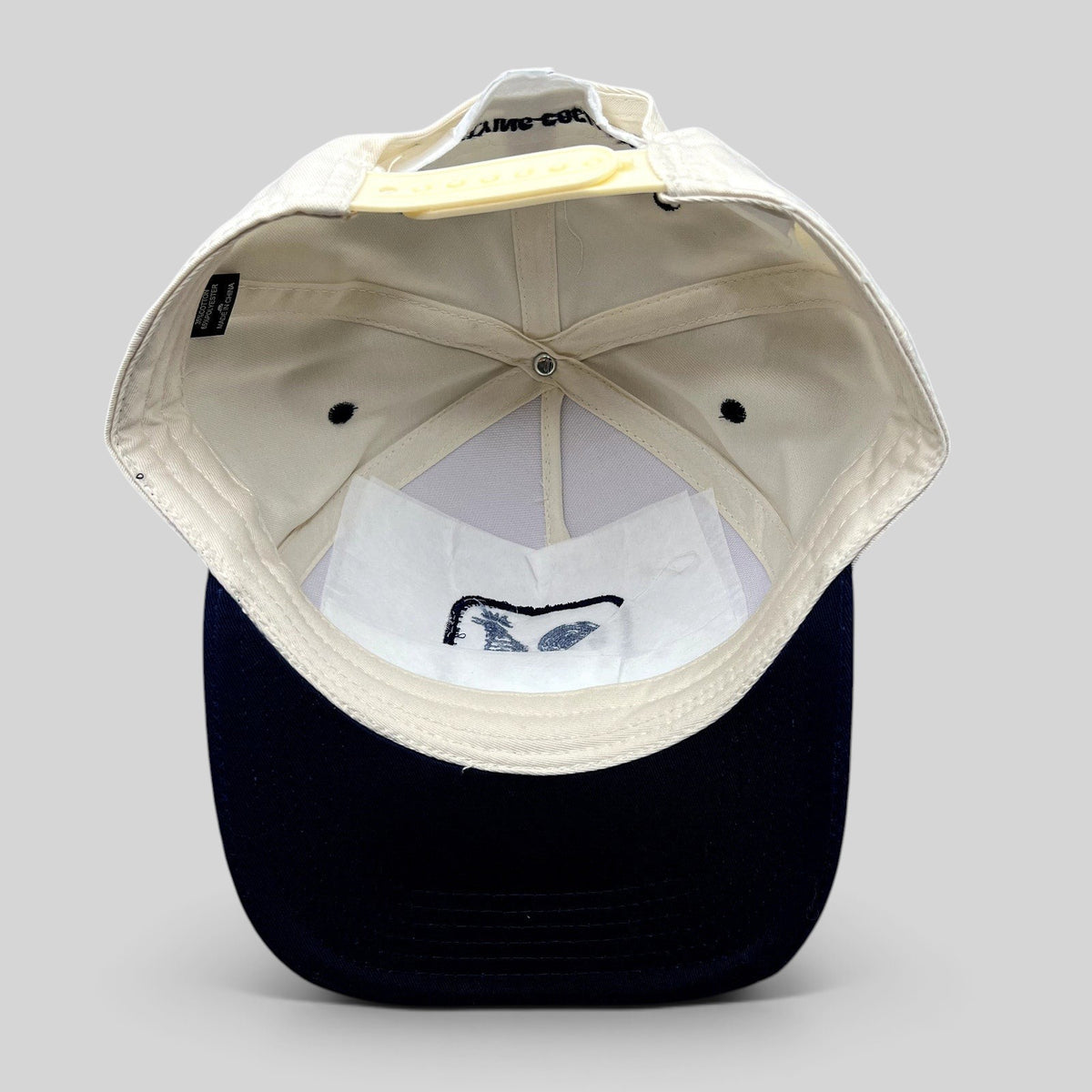 Raree Finds The Flying Cock NYC snapback hat interior view showing cream crown, navy brim, and adjustable strap