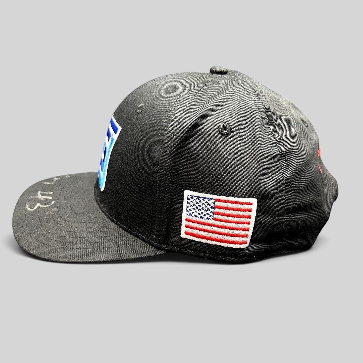 Raree Finds black snapback racing hat with embroidered Spears logo, American flag patch, and silver autograph on brim.