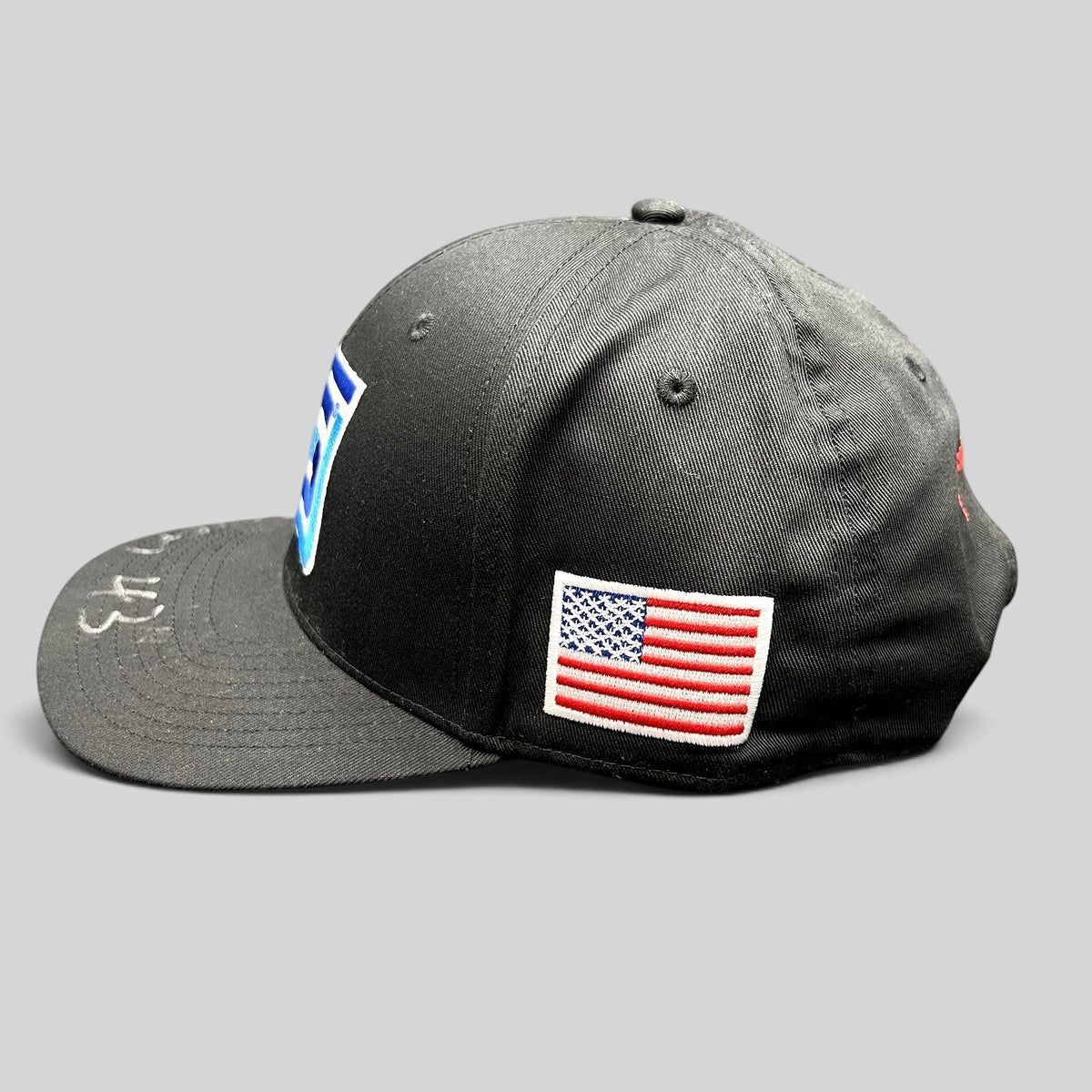 Raree Finds black snapback racing hat with embroidered Spears logo, American flag patch, and silver autograph on brim.