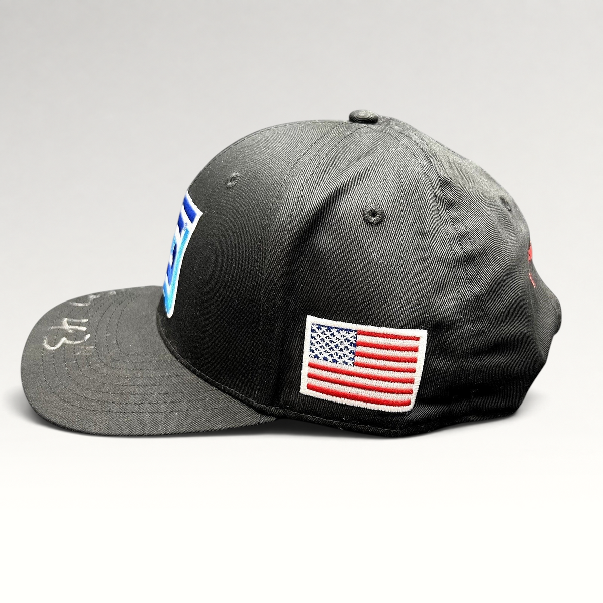Raree Finds black snapback racing hat with embroidered Spears logo, American flag patch, and silver autograph on brim.
