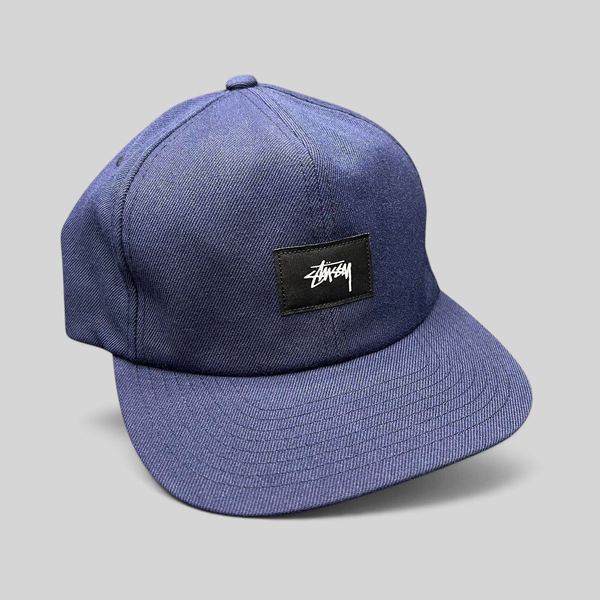 Raree Finds navy Stussy strapback hat with a black box logo patch and white script embroidery on a flat brim cap.