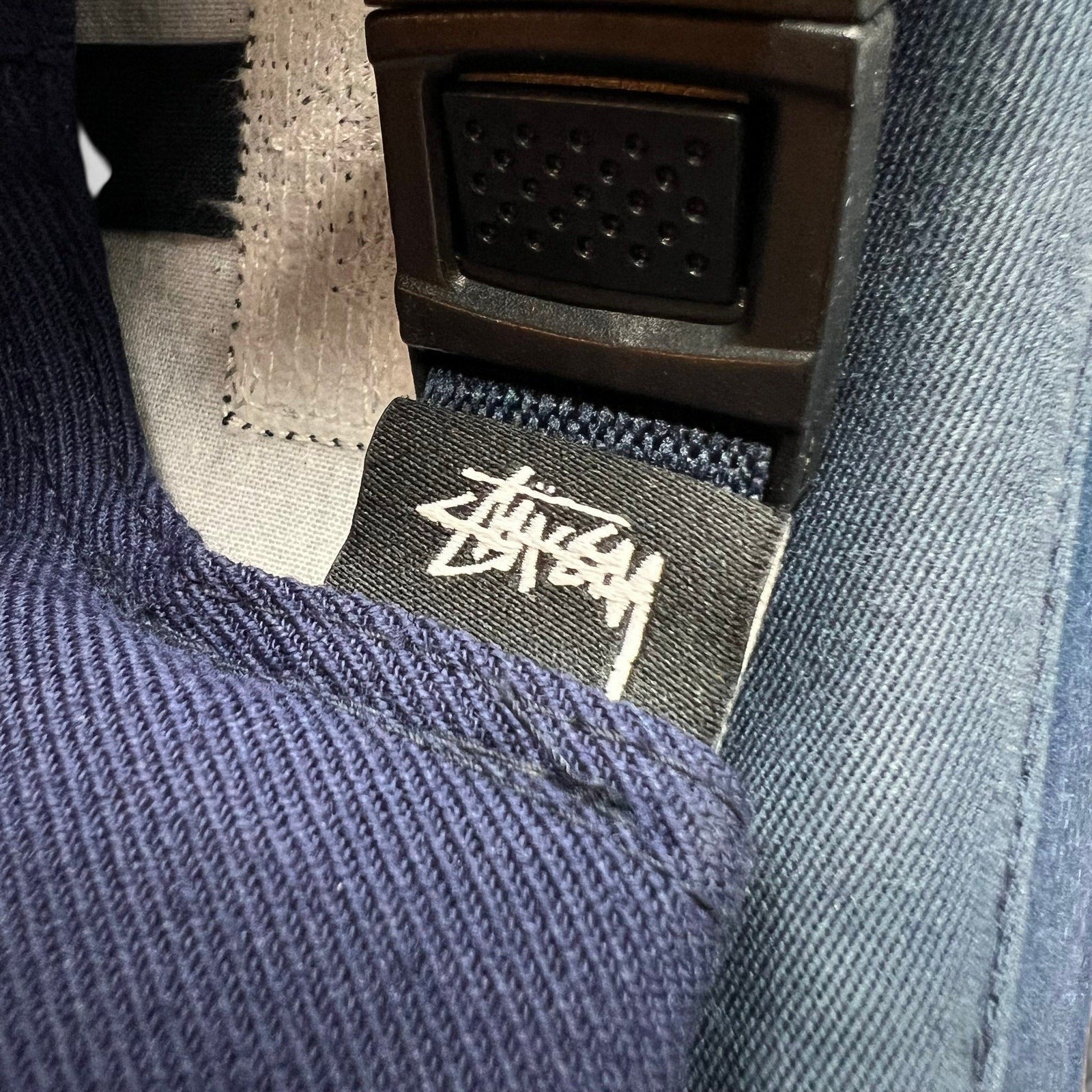 Raree Finds navy Stussy strapback hat featuring a black interior fabric tag with white signature script logo