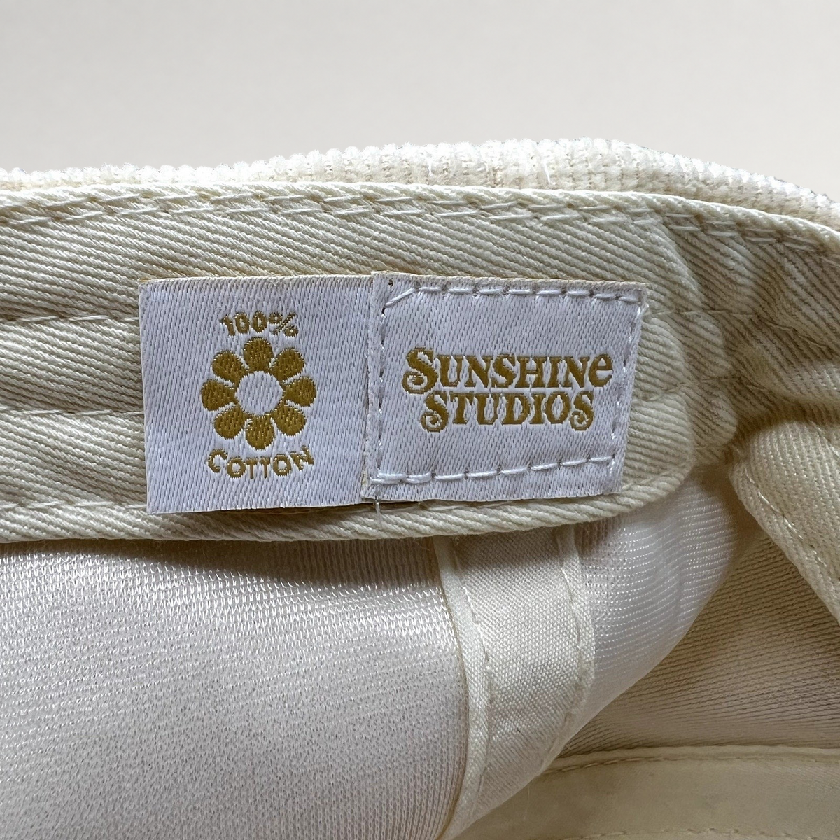 Raree Finds Sunshine Studios cream corduroy hat interior label with 100% cotton flower logo and brand text