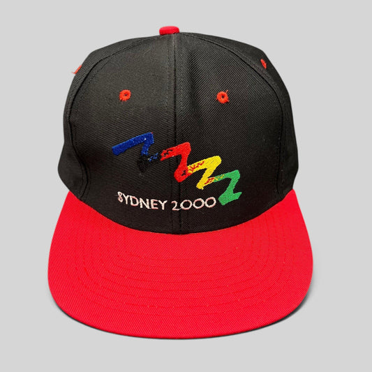 Raree Finds vintage Sydney 2000 Olympics snapback hat with black crown, red brim, and multicolor embroidered logo.