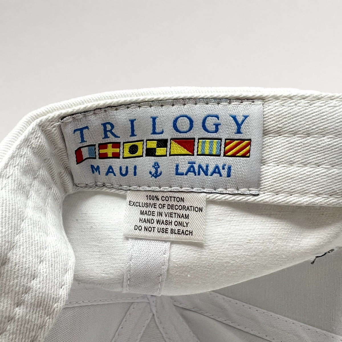 Raree Finds white cotton cap interior label featuring Trilogy Maui Lana‘i branding and nautical signal flags