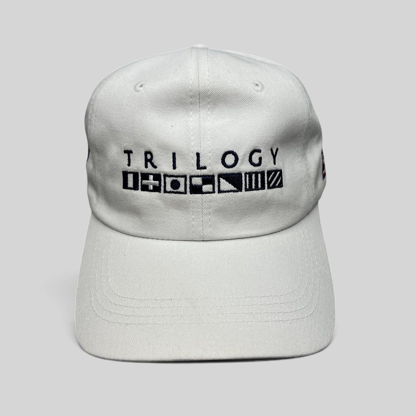 Raree Finds white cotton strapback cap featuring Trilogy branding and embroidered nautical signal flags on the front.