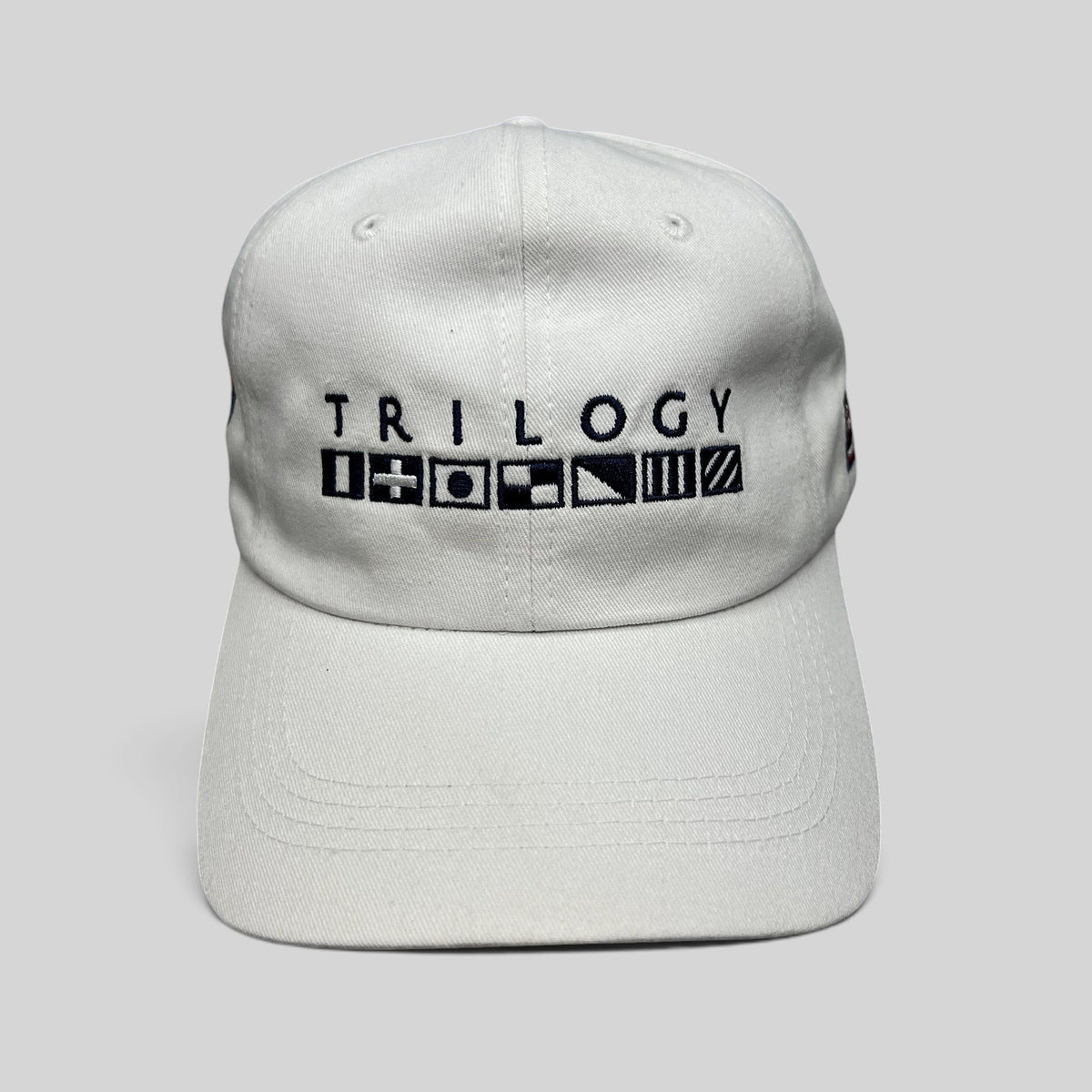 Raree Finds white cotton strapback cap featuring Trilogy branding and embroidered nautical signal flags on the front.