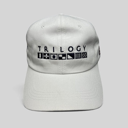 Raree Finds white cotton strapback cap featuring Trilogy branding and embroidered nautical signal flags on the front.