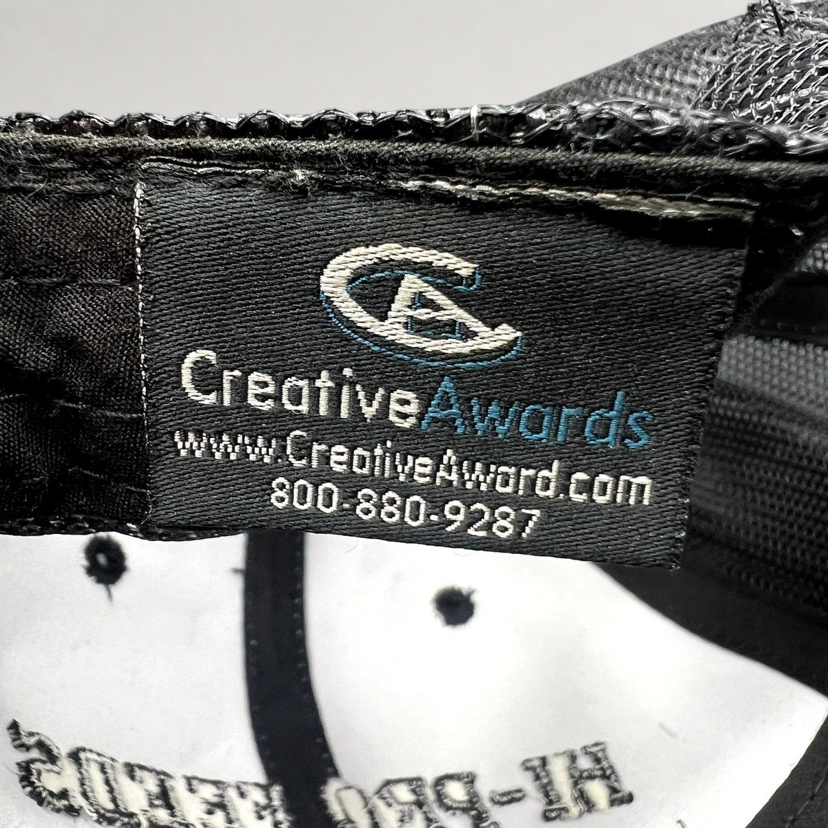 Raree Finds branded trucker hat interior tag showing Creative Awards manufacturer logo and contact information