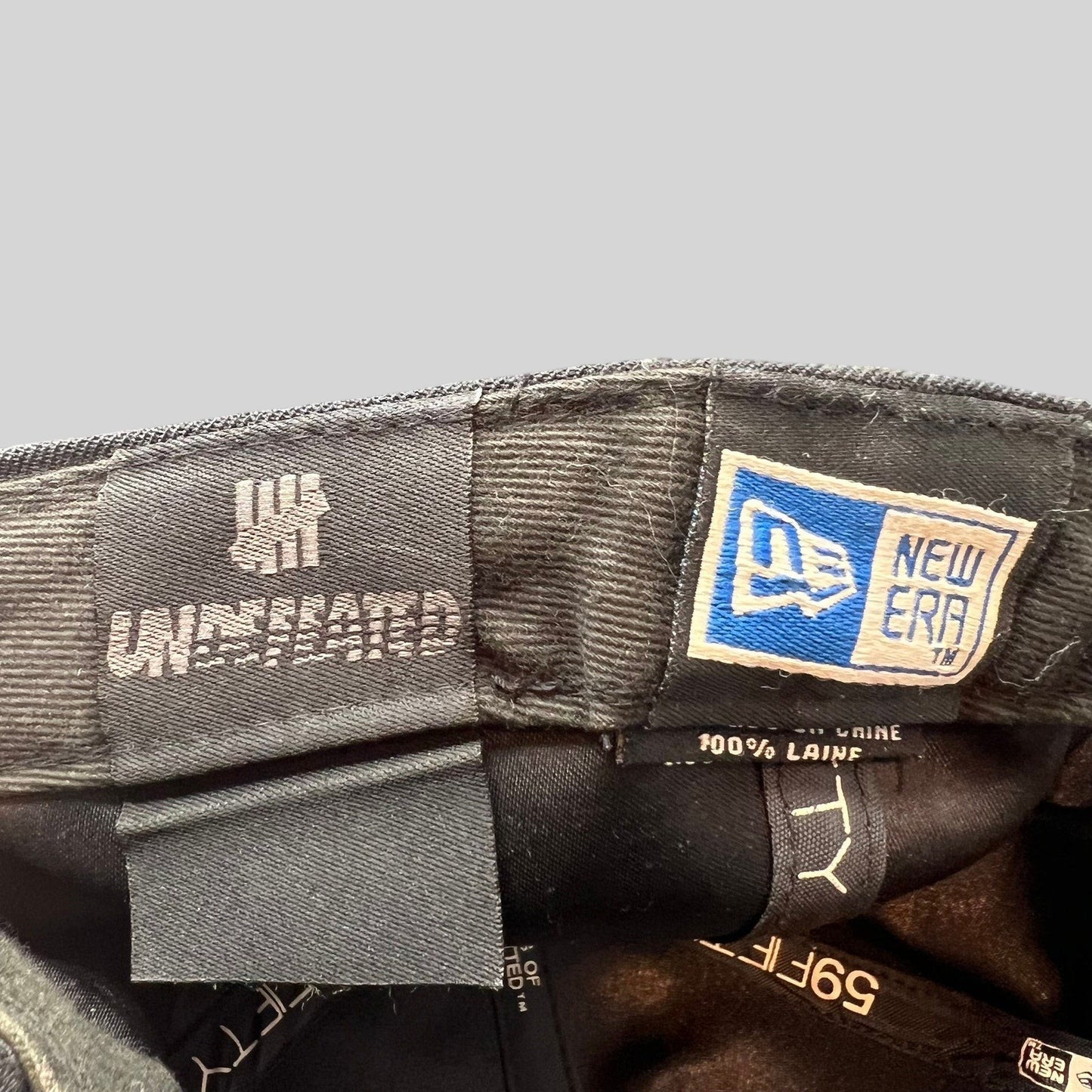 Raree Finds Undefeated New Era 59FIFTY wool cap interior tags showing brand logos and 100 percent wool material