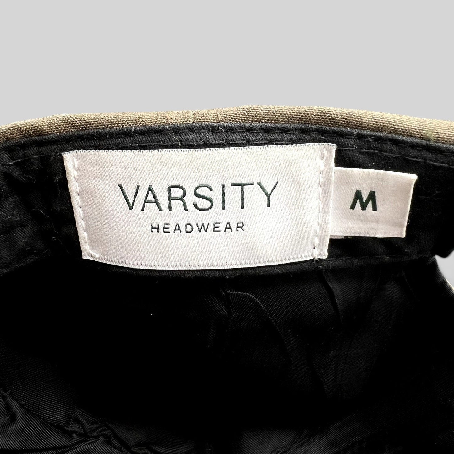 Raree Finds Varsity Headwear cap interior showing white brand label and size M tag against brown structured crown