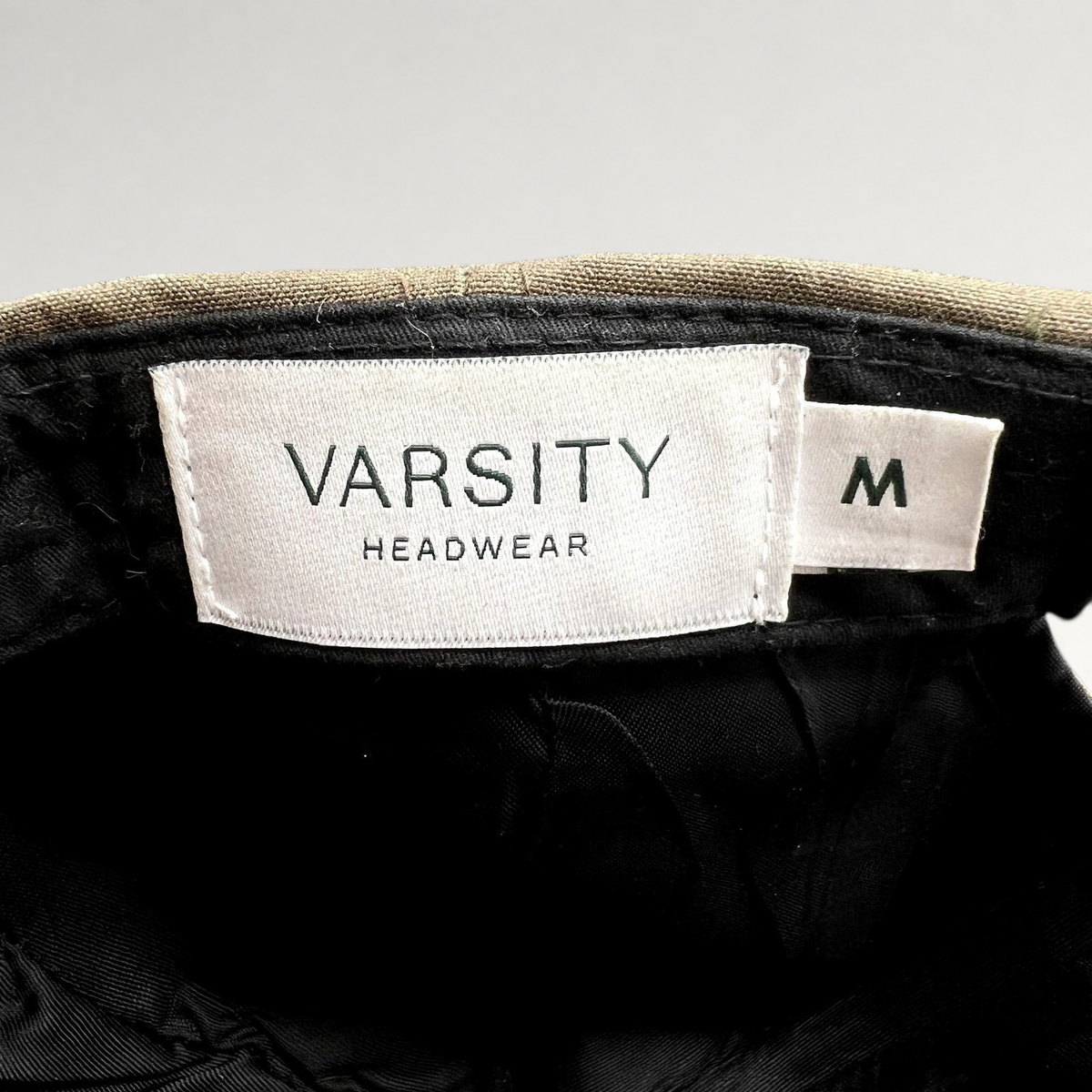 Raree Finds Varsity Headwear cap interior showing white brand label and size M tag against brown structured crown