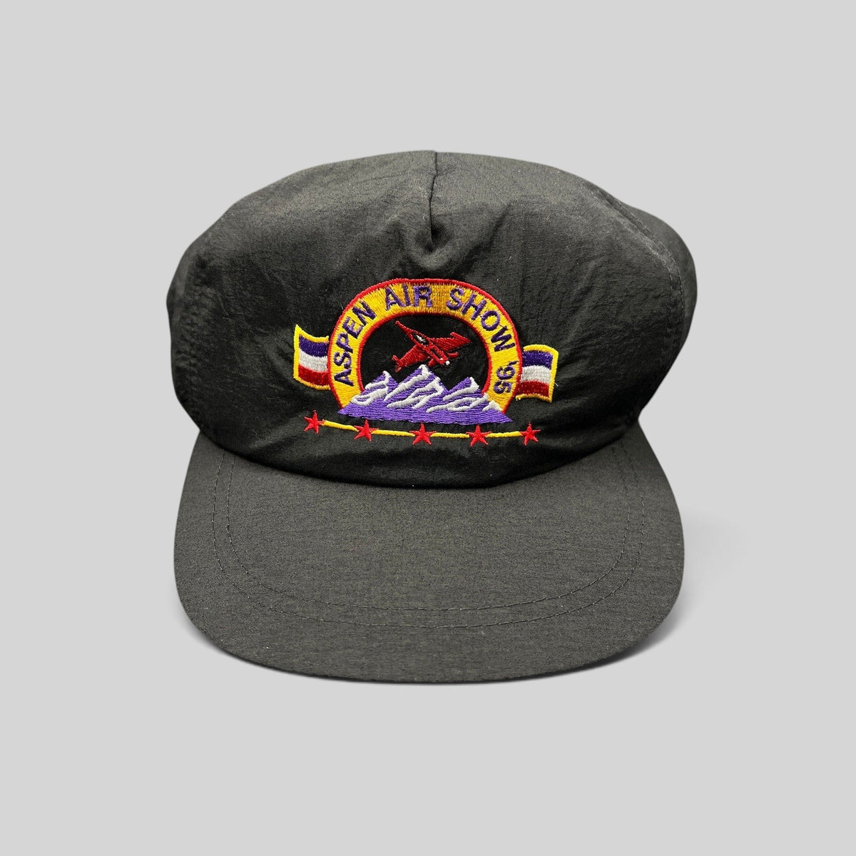 Raree Finds vintage 1995 Aspen Air Show black nylon snapback hat with multicolor embroidered jet and mountain design.