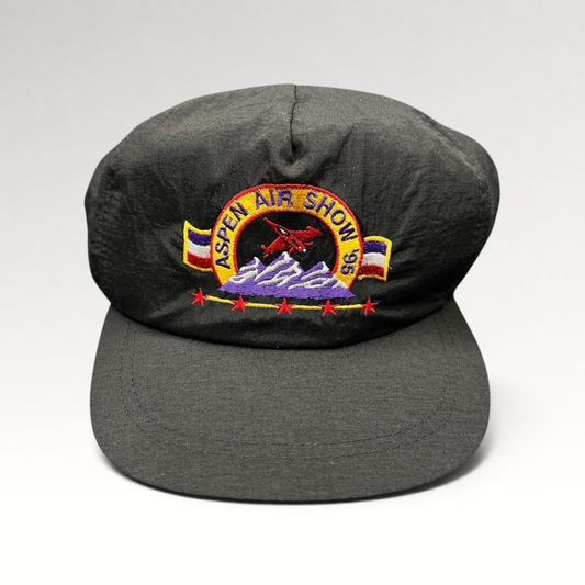 Raree Finds vintage 1995 Aspen Air Show black nylon snapback hat with multicolor embroidered jet and mountain design.