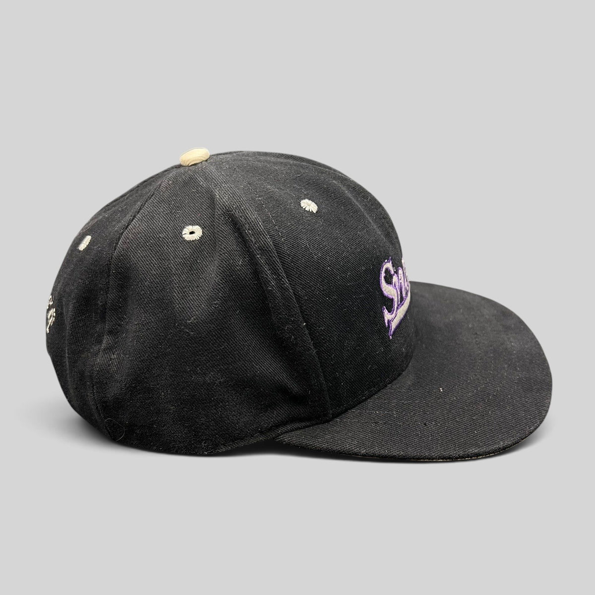 Raree Finds vintage 90s black snapback hat with purple script embroidery and a light gray brim, side profile view.
