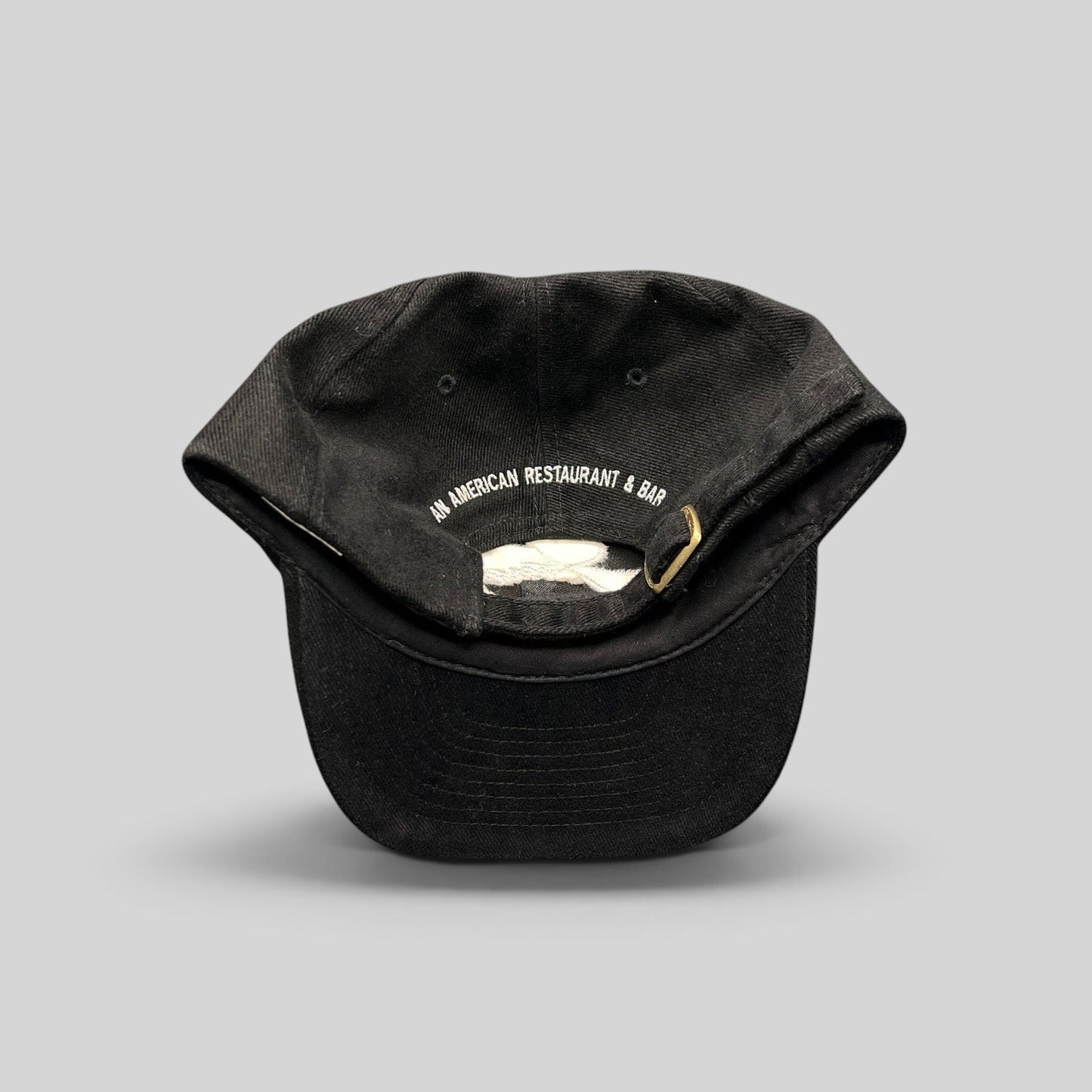 Raree Finds vintage black cotton strapback hat with white embroidered text on the back and brass-tone buckle closure.