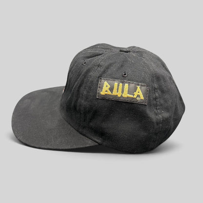 Raree Finds vintage 90s black cotton BULA snapback hat with gold embroidered logo, USA Ski Team memorabilia style.