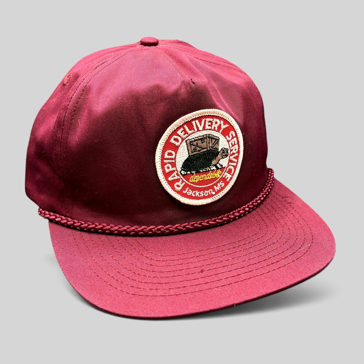 Raree Finds vintage burgundy trucker hat with a Rapid Delivery Service embroidered patch and braided rope brim detail.