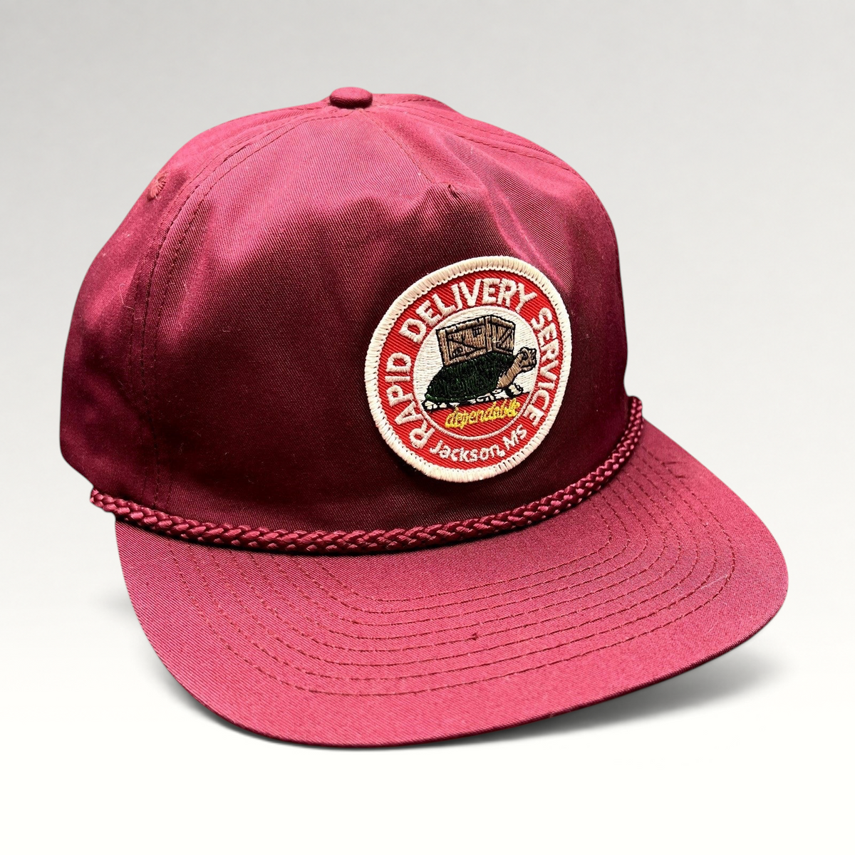Raree Finds vintage burgundy trucker hat with a Rapid Delivery Service embroidered patch and braided rope brim detail.