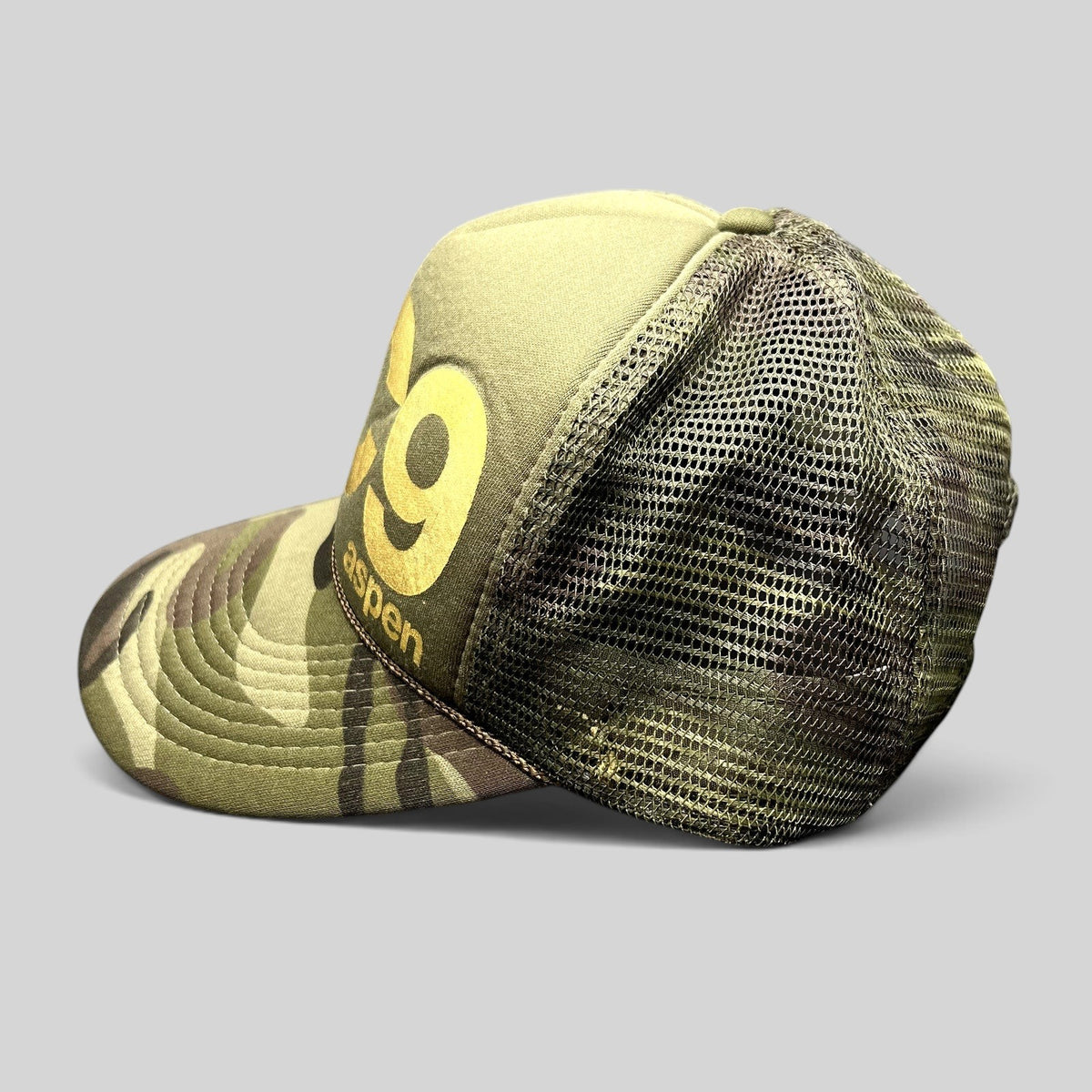Raree Finds vintage Cloud 9 Aspen trucker hat in olive and camo with gold print, rope detail, and mesh back.