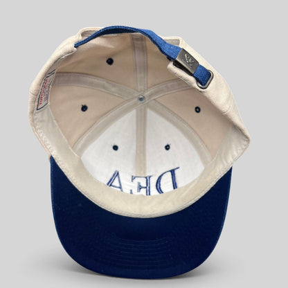 Raree Finds vintage Yupoong DEA cotton strapback hat with tan crown, navy blue brim, and adjustable metal buckle