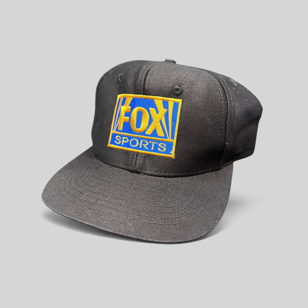 Raree Finds vintage 90s black cotton snapback hat featuring an embroidered gold and royal blue FOX Sports logo.