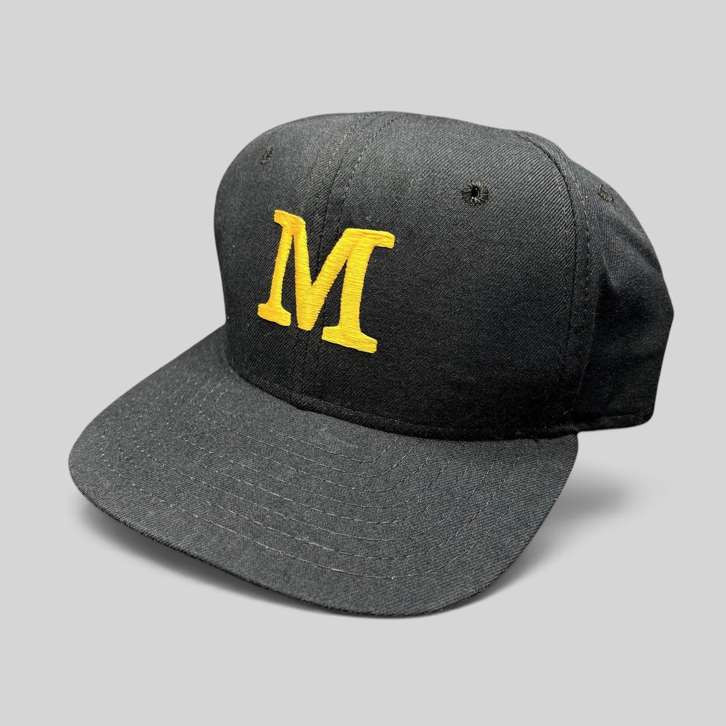 Raree Finds vintage New Era snapback hat in black with a gold embroidered M logo on the structured front crown
