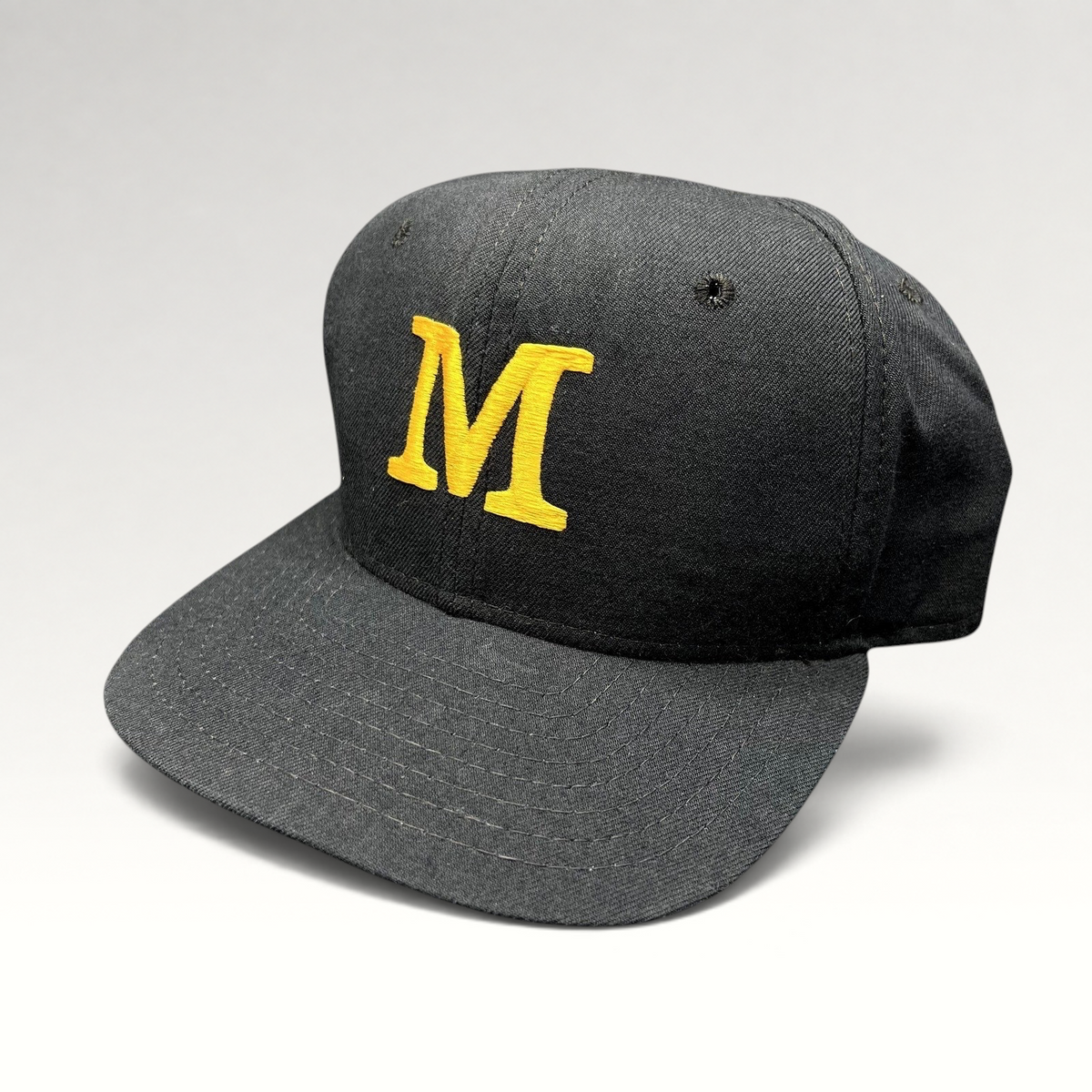 Raree Finds vintage New Era snapback hat in black with a gold embroidered M logo on the structured front crown