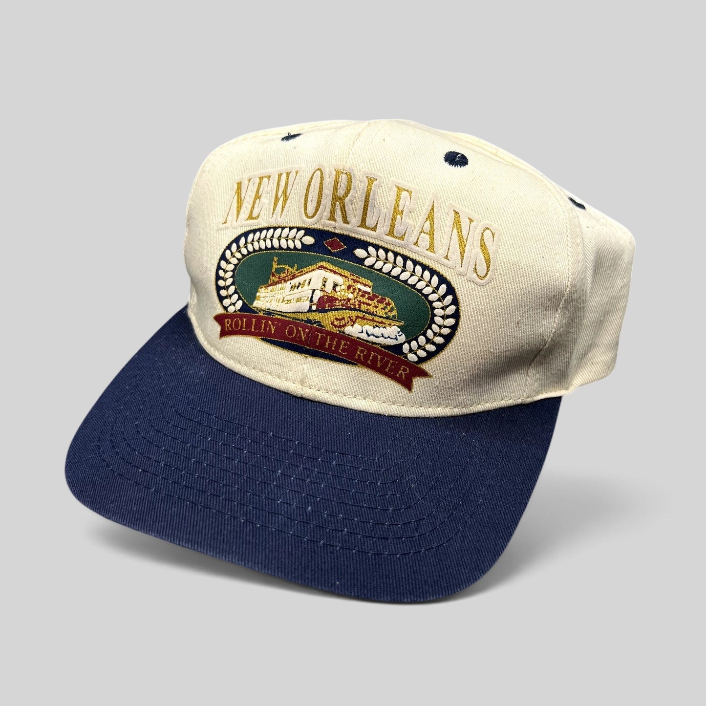 Raree Finds vintage New Orleans snapback hat with embroidered riverboat graphic, cream crown, and navy blue brim.