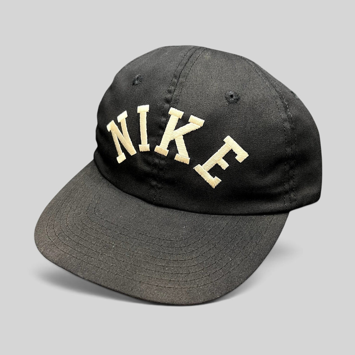 Raree Finds vintage black Nike strapback hat with an oversized arched embroidered logo and a green undervisor.