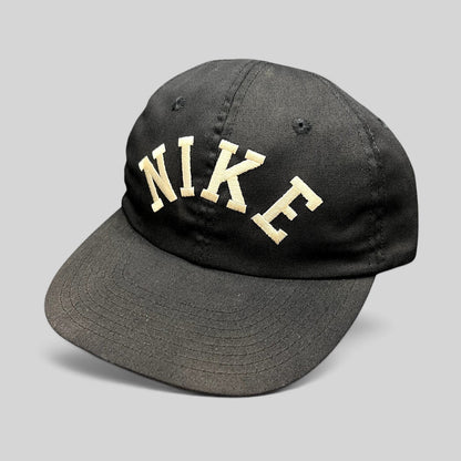 Raree Finds vintage black Nike strapback hat with an oversized arched embroidered logo and a green undervisor.