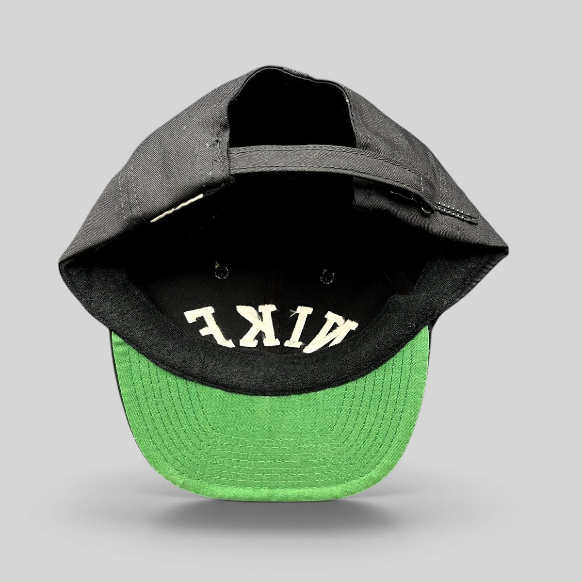 Raree Finds vintage black Nike strapback hat with green undervisor and embroidered arch logo, seen from above.