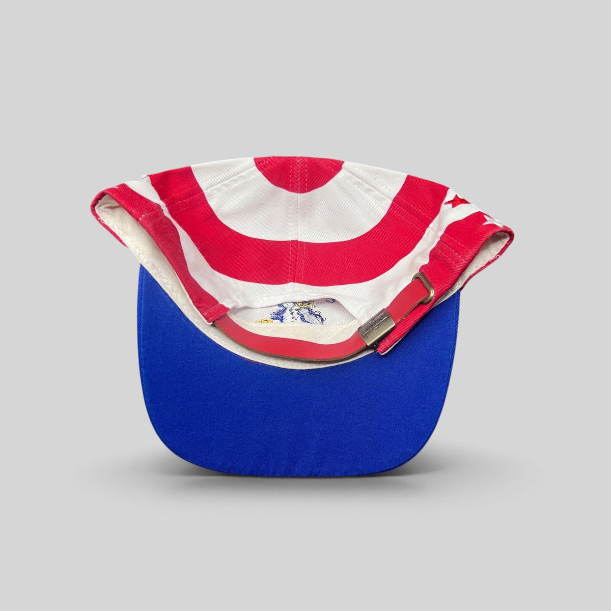 Raree Finds vintage Nissin Cap patriotic baseball hat with red and white stripes, blue brim, and brass buckle strap.