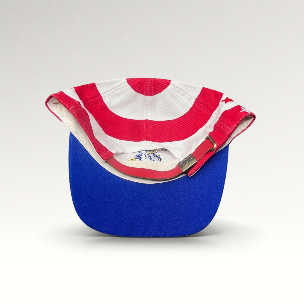 Raree Finds vintage Nissin Cap patriotic baseball hat with red and white stripes, blue brim, and brass buckle strap.