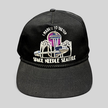Raree Finds vintage 90s black snapback hat featuring an embroidered Seattle Space Needle graphic and braided rope trim.