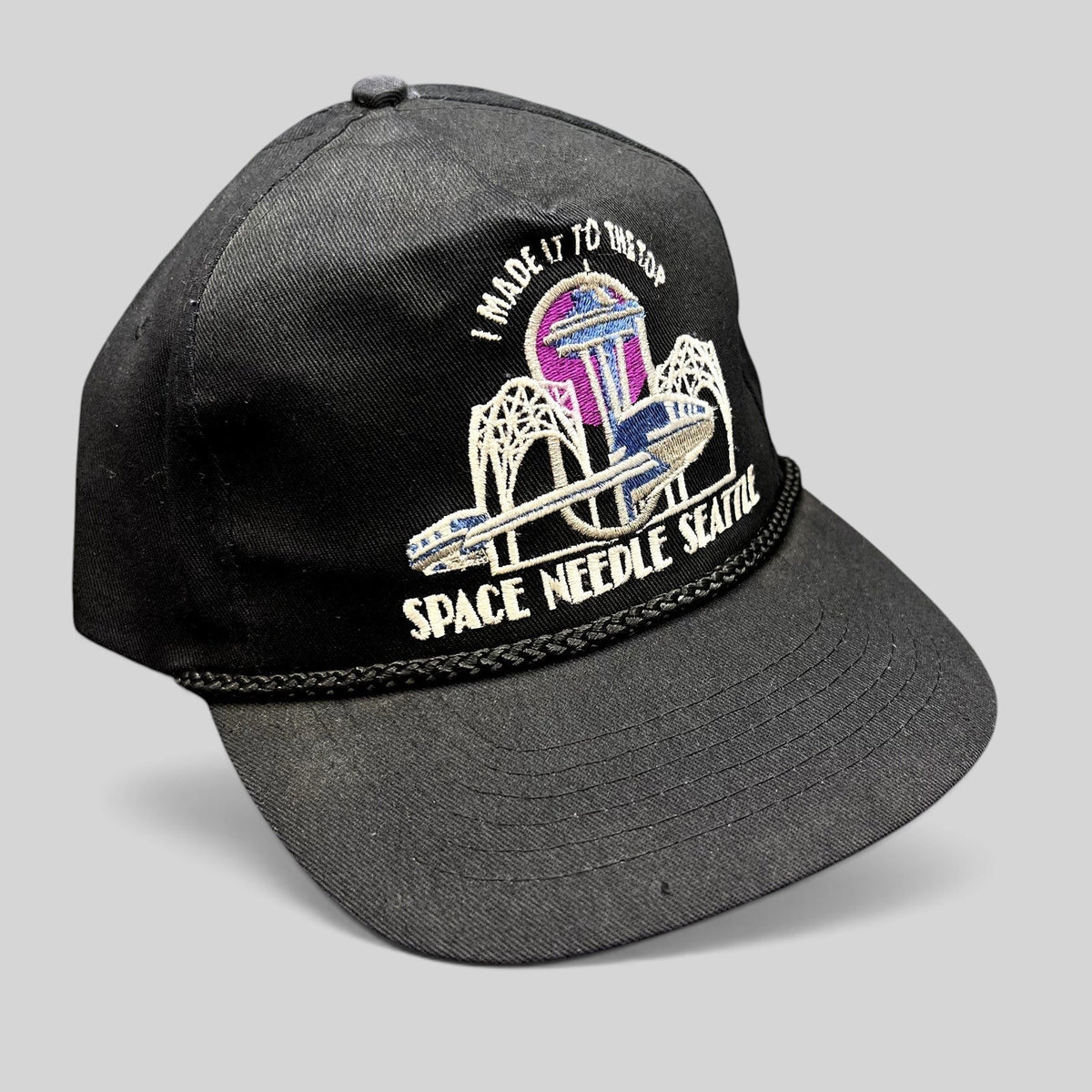 Raree Finds vintage 90s black snapback hat with embroidered Seattle Space Needle graphic and braided rope bill detail.