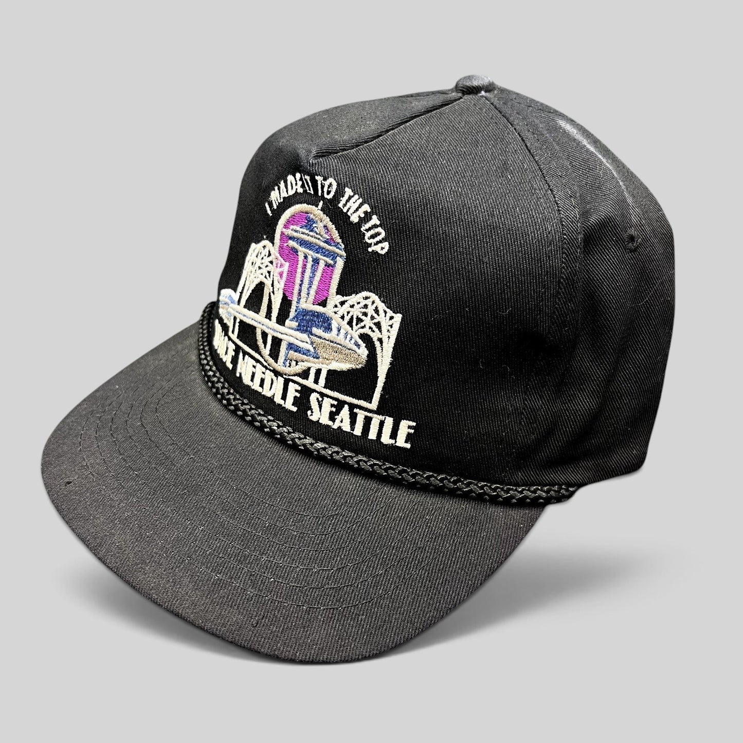Raree Finds vintage 90s black snapback hat featuring a colorful Seattle Space Needle embroidery and braided rope trim.
